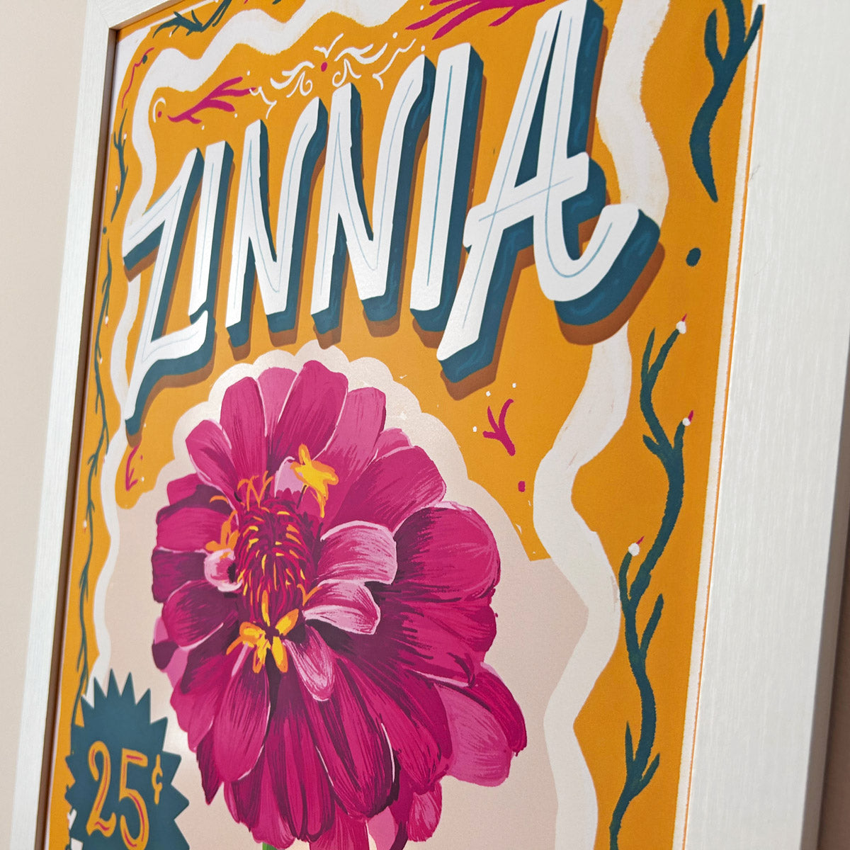 Close up of framed artwork with a large pink flower and the word 'Zinnia' on an burnt orange background.