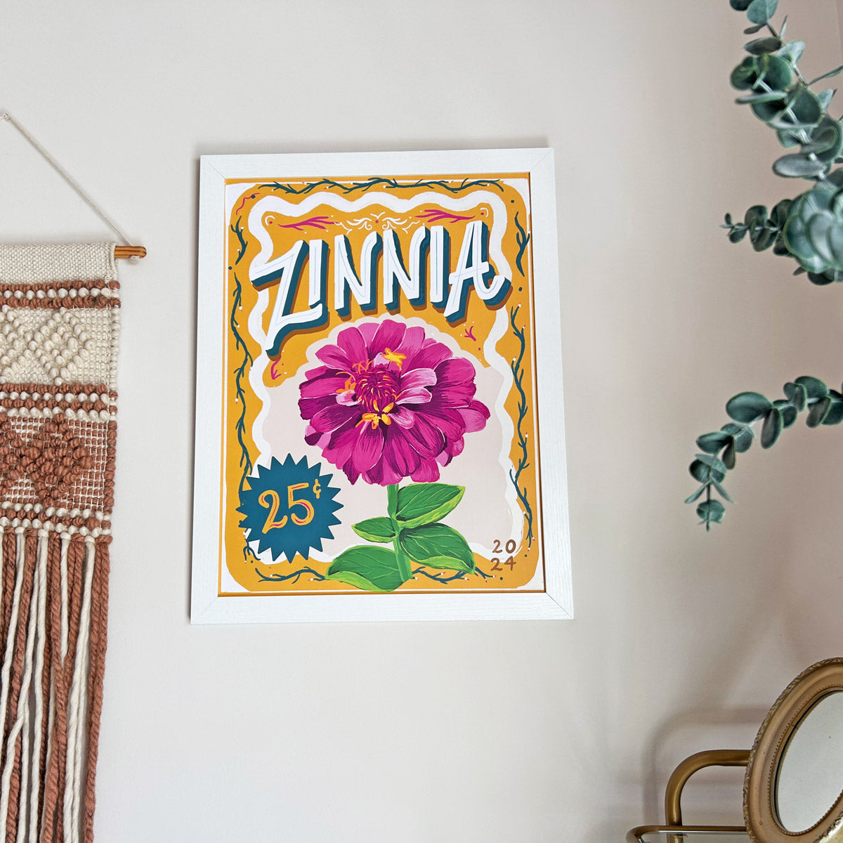 Framed artwork of a zinnia flower on a wall with decorative elements around it