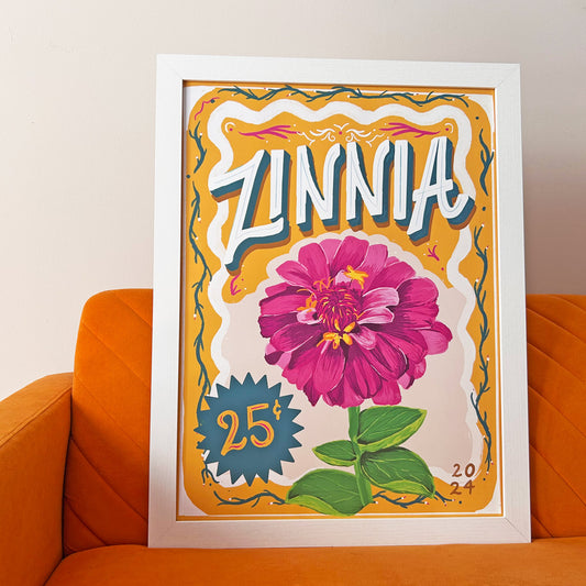 Framed artwork of a zinnia flower with decorative elements on an orange couch.